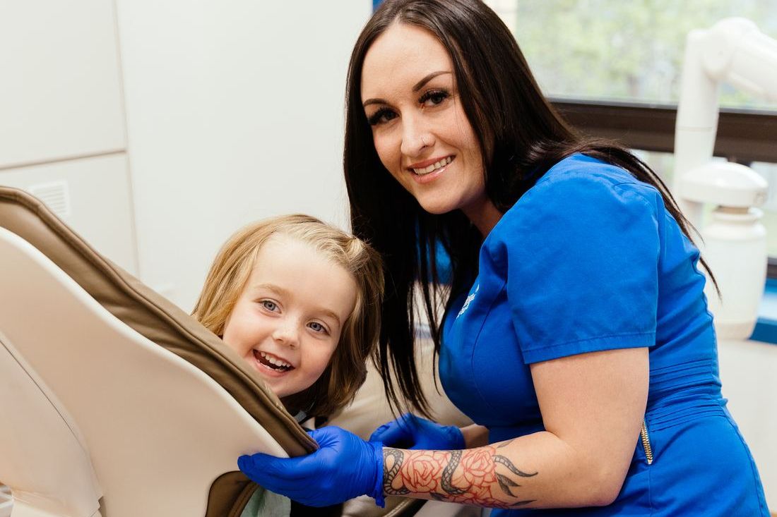 A Norwood Dental hygienist smiling with a young child in the dental chair